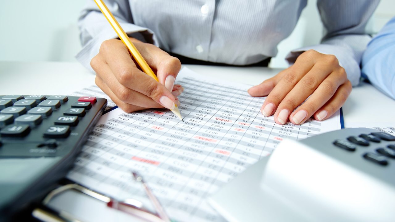 Photo of human hands holding pencil and ticking data in documents